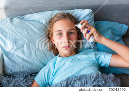 Sick teenage little girl with high fever and headache laying in bed checking her temperature Sick teenage little girl with high fever and headache laying in bed checking her temperature 70243592