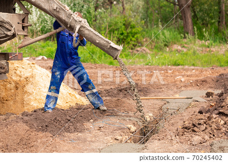 Construction worker laying cement or concrete into the foundation formwork 70245402