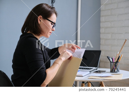 Mature woman opening envelope with paper documents 70245441