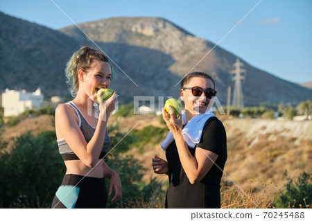 Two women mother and teenage daughter eating green apples on nature 70245488