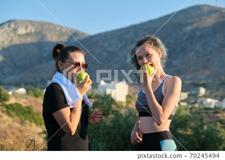Family mother and daughter eating apples after exercise, jogging in nature Family mother and daughter eating apples after exercise, jogging in nature 70245494