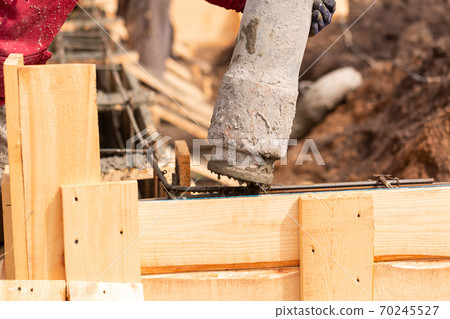 Close up of construction worker laying cement or concrete into the foundation formwork with automatic pump 70245527