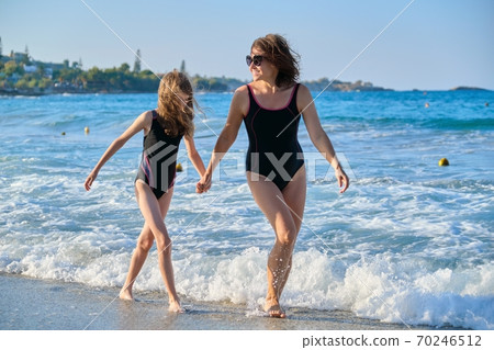 Mother and daughter child walking together on beach holding hands Mother and daughter child walking together on beach holding hands 70246512