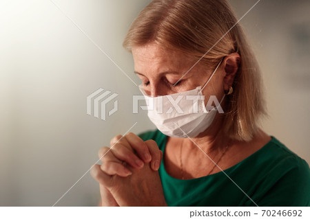 Woman in face mask praying for sick patient Woman in face mask praying for sick patient 70246692