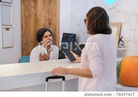 Resort hotel front desk, woman guest talking to man working at reception Resort hotel front desk, woman guest talking to man working at reception 70247427