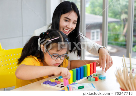 Asian girl with Down's syndrome play puzzle toy with her teacher in classroom. Asian girl with Down's syndrome play puzzle toy with her teacher in classroom. 70247713