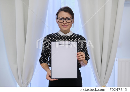 Mature smiling successful business woman showing blank paper on clipboard Mature smiling successful business woman showing blank paper on clipboard 70247843