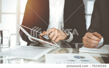 Business people using tablet computer while working together in sunny office. Unknown businessman sitting at the desk with his partner 70248388