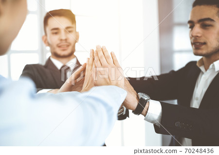 Business people group showing teamwork, joining hands and giving five to each other in sunny office 70248436