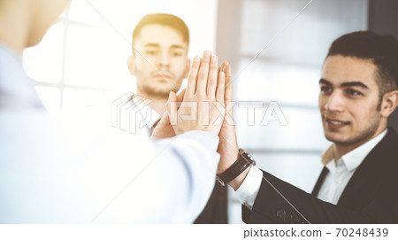 Business people group showing teamwork, joining hands and giving five to each other in sunny office 70248439