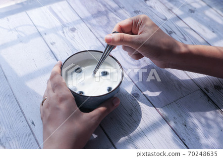 women hand eating fresh yogurt with blue berry in a bowl  70248635