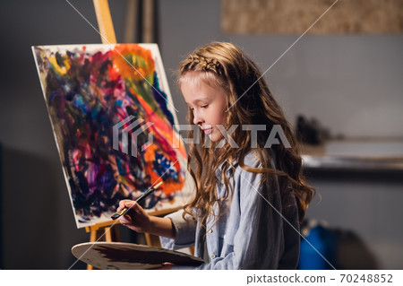 Abstract painting lesson. A little cute girl writes a color picture in oil or acrylic technique. Abstract painting lesson. A little cute girl writes a color picture in oil or acrylic technique. 70248852