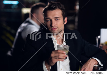 portrait of a young man in a shirt and jacket at the bar with a cocktail in his hands portrait of a young man in a shirt and jacket at the bar with a cocktail in his hands 70248860