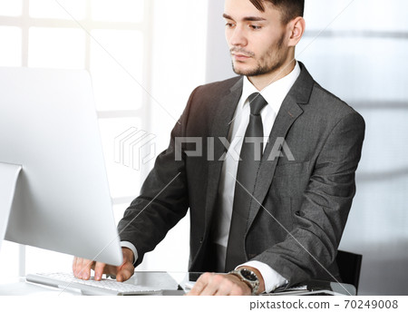 Businessman working with computer in sunny office. Headshot of male entrepreneur at workplace. Business concept Businessman working with computer in sunny office. Headshot of male entrepreneur at workplace. Business concept 70249008