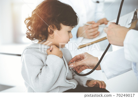 Woman-doctor examining a child patient by stethoscope in sunny clinik. Cute arab toddler at physician appointment Woman-doctor examining a child patient by stethoscope in sunny clinik. Cute arab toddler at physician appointment 70249017