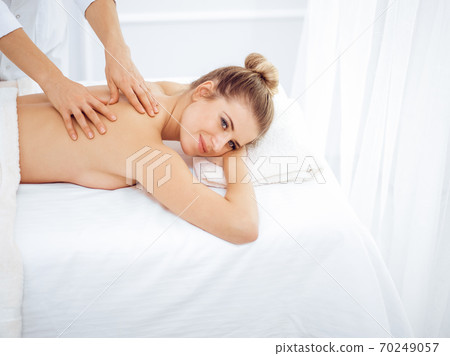 Young and blonde woman enjoying massage of back in spa salon. Beauty concept 70249057