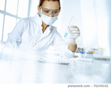 Female laboratory assistant analyzing test tube with blue liquid. Medicine, health care and researching concept Female laboratory assistant analyzing test tube with blue liquid. Medicine, health care and researching concept 70249102