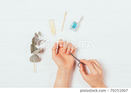 Top view of female hands doing manicure using scissors Top view of female hands doing manicure using scissors 70251007