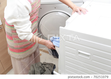 Housewife putting clothes in a drum-type washing machine Housewife putting clothes in a drum-type washing machine 70251079