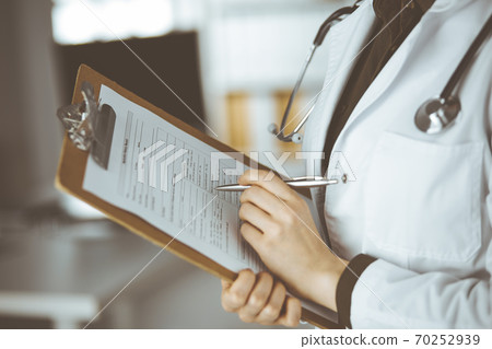 Unknown female doctor using clipboard in clinic. Perfect medical service in hospital Unknown female doctor using clipboard in clinic. Perfect medical service in hospital 70252939