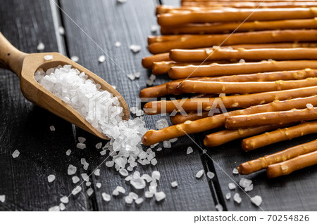 Salty sticks. Crunchy pretzels and coarse salt in wooden scoop. 70254826