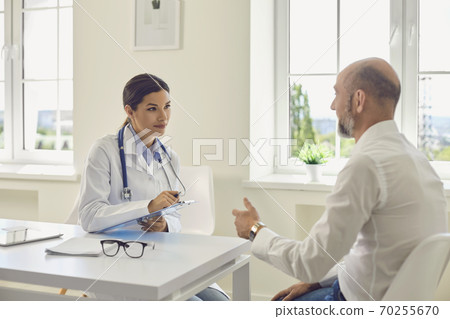 Male patient pensioner speaks with the doctor at the desk in the office of the hospital. Male patient pensioner speaks with the doctor at the desk in the office of the hospital. 70255670