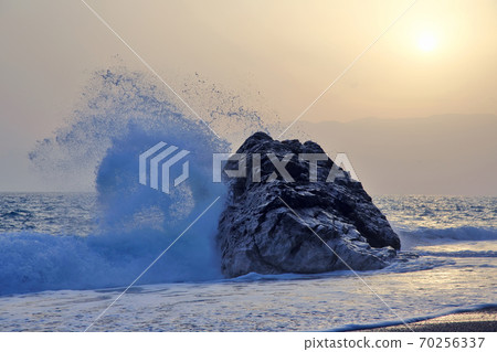 Sea wave beating with force against the rock at sunset 70256337