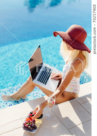 woman using laptop and work remotely near swimming pool 70257908