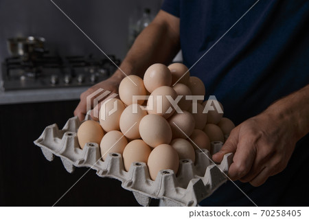 a man holding a full tray of chicken eggs in his own kitchen a man holding a full tray of chicken eggs in his own kitchen 70258405