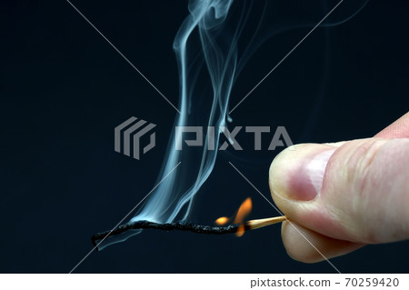 Burning and smoking wooden match in hand on dark background Burning and smoking wooden match in hand on dark background 70259420