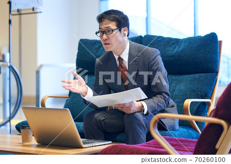 Middle businessman sitting on the sofa and having an online meeting Middle businessman sitting on the sofa and having an online meeting 70260100