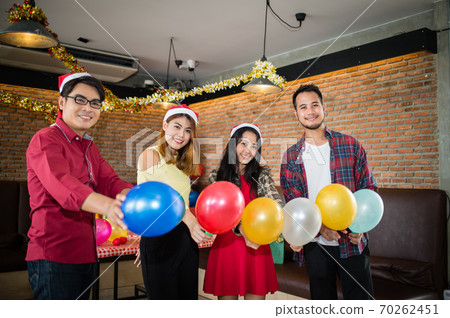 Asian man and woman having fun in Christmas party, they holding balloons on hand and looking to camera, Concept of Christmas party or New Year's party. 70262451
