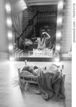 newborn photo shoot: a small child is lying on a wooden bed under a blanket. the photographer's reflection in the mirror newborn photo shoot: a small child is lying on a wooden bed under a blanket. the photographer's reflection in the mirror 70263219