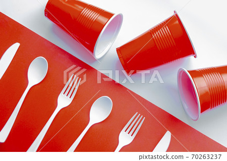Horizontal view of single use white plastic cutlery and red plastic glass on a red and white background. Concept Horizontal view of single use white plastic cutlery and red plastic glass on a red and white background. Concept 70263237