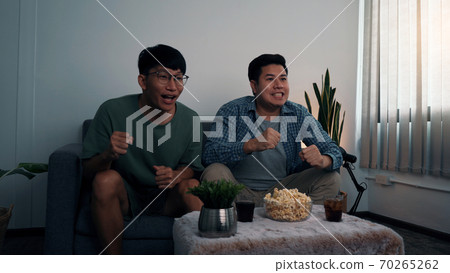 Asian male friends sit and win their favorite team that is broadcasting live football matches. Asian male friends sit and win their favorite team that is broadcasting live football matches. 70265262