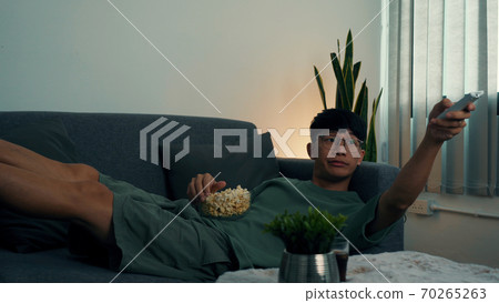 Asian guy is relaxing for the weekend by watching series his home at night. 70265263