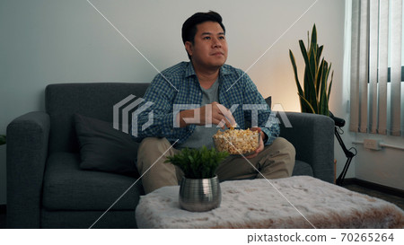 Asian guy is relaxing for the weekend by watching series his home at night. Asian guy is relaxing for the weekend by watching series his home at night. 70265264