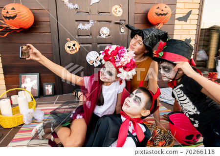 Cute halloween girl with smartphone making selfie with two boys and young woman Cute halloween girl with smartphone making selfie with two boys and young woman 70266118