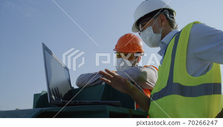 Engineers in masks using laptop on construction site Engineers in masks using laptop on construction site 70266247