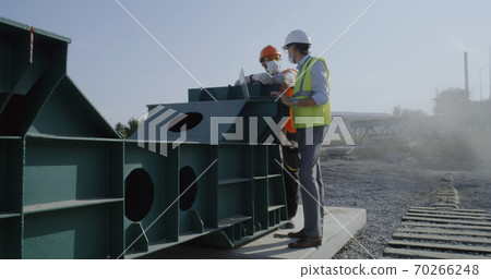 Engineers in masks using laptop on construction site Engineers in masks using laptop on construction site 70266248