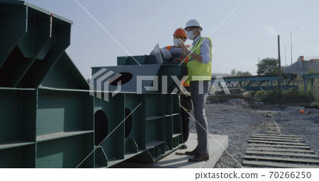 Engineers in masks using laptop on construction site Engineers in masks using laptop on construction site 70266250