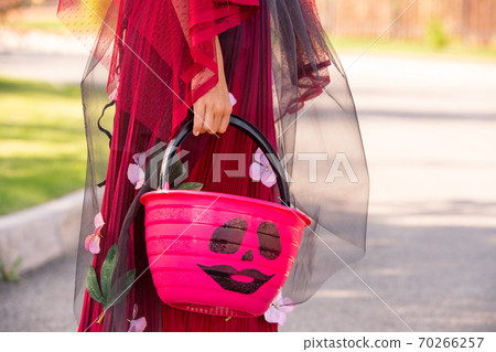 Hand of little girl in costume of halloween witch holding pink plastic basket Hand of little girl in costume of halloween witch holding pink plastic basket 70266257
