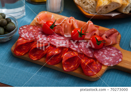 Spanish tasty meal slicing sausages and ham with tomatoes at wooden desk 70273000
