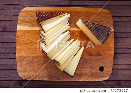 Sliced wedge of aged sheep cheese on wooden board 70273317