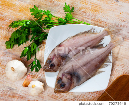 Uncooked roosterfish with greens and garlic on wooden board 70273646