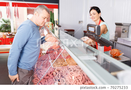 Seller helping male choosing sausages in shop Seller helping male choosing sausages in shop 70275233