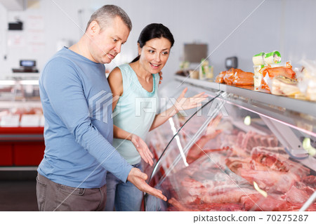 Glad couple choosing meat and discussing 70275287