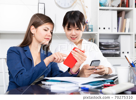 Two women write sms by phone in the office Two women write sms by phone in the office 70275310