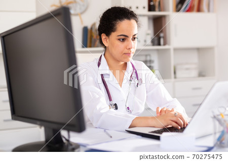 Female doctor working on laptop in office Female doctor working on laptop in office 70275475
