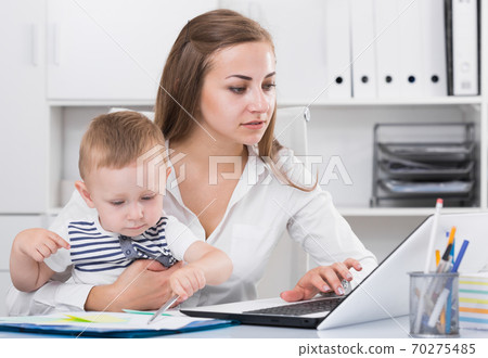 Satisfied mother with child is productively working behind laptop 70275485